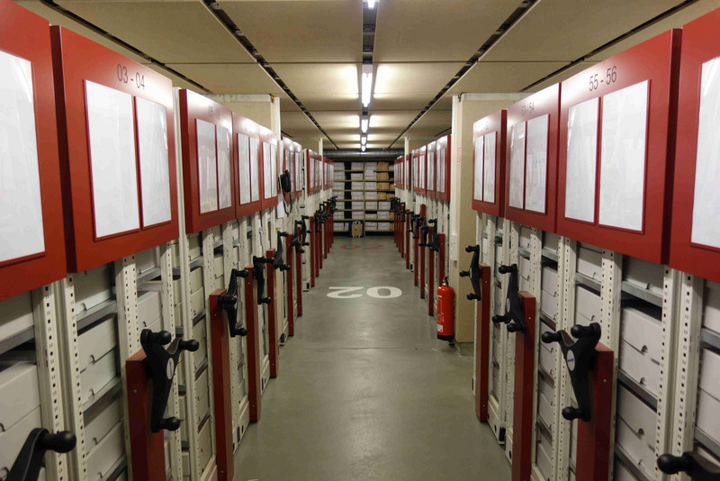Blick in einen Magazingang mit Rollregalen auf der linken und rechten Seite