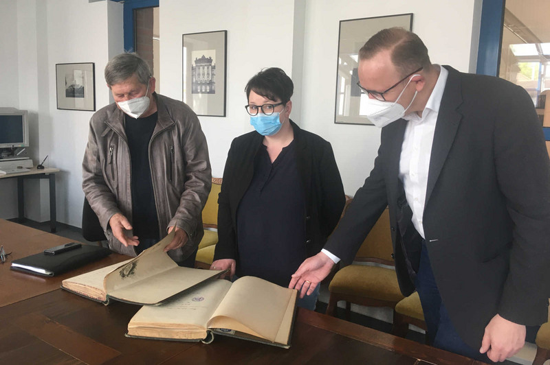 Wolfgang Finze, Stephanie Göring und Dr. Hermann Kinne blättern in den auf einem Tisch ausliegenden Zechbüchern. 