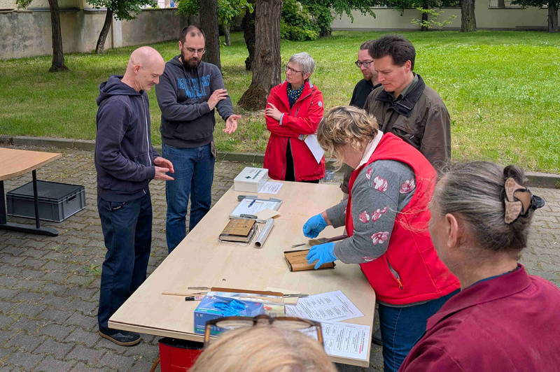 Teilnehmende während der Notfallübung behandeln durchfeuchtetes Archivgut an einem Tisch im Außenbereich des Landesarchivs in Merseburg