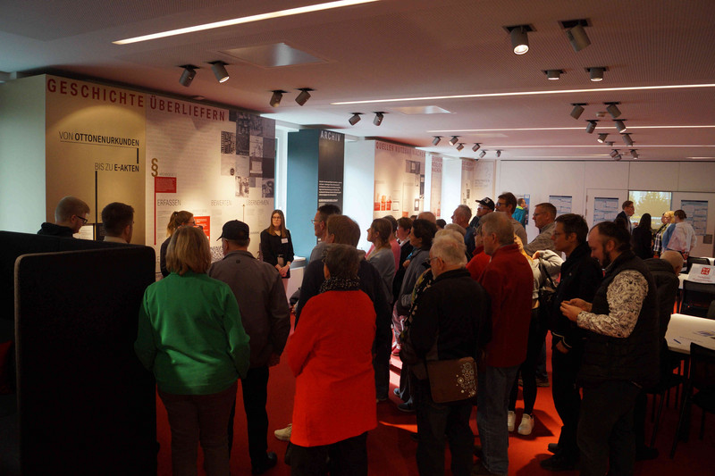 Blick in den Ausstellungsraum während einer Führung. Das Publikum steht vor einer Wandtafel. 
