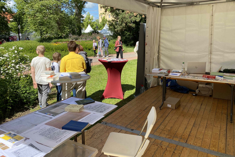 Zwei Tische mit Informationsmaterialien und Ausdrucken von Archivquellen (Handschriften, Karten), Blick nach draußen zeigt Personen im Gespräch