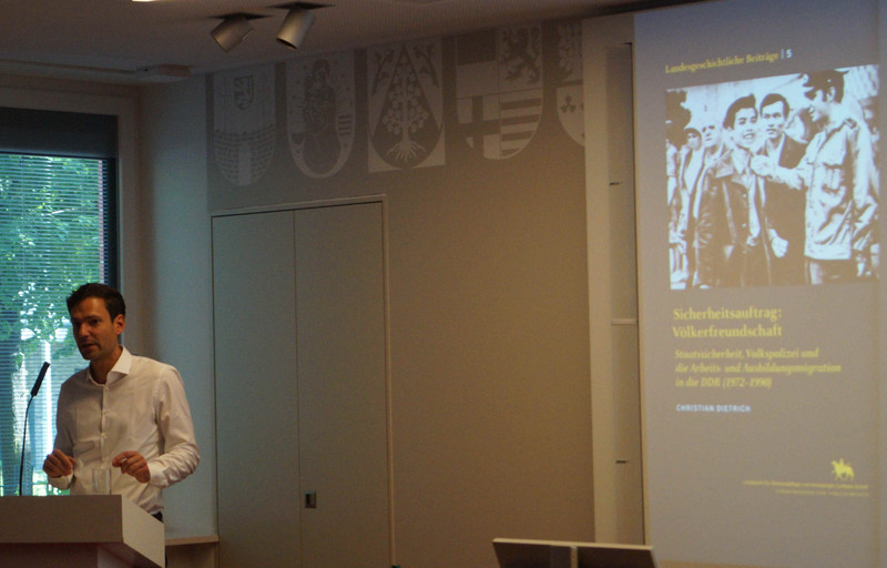 Mann am Rednerpult im Hintergrund Leinwand mit Bild der wissenschaftlichen Studie